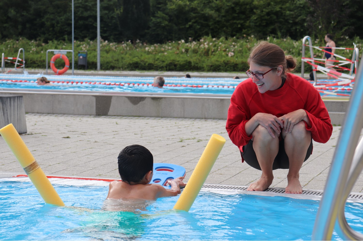 Eine Schwimmausbilderin spricht mit einem Kind mit Poolnoodle